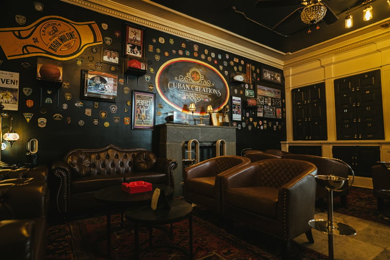 The Cuban Creations front lounge in New Orleans with leather Chesterfield seating, the gold oval sign and a wall of collected badges